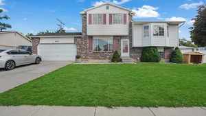 Tri-level home featuring brick siding, an attached garage, driveway, and a front lawn