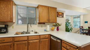 Kitchen featuring stainless steel dishwasher, a peninsula, light countertops, and brown cabinets