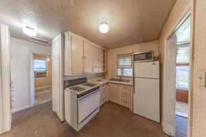 Kitchen featuring white appliances, carpet flooring, a textured ceiling, plenty of natural light, and cooling unit