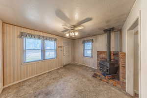 Unfurnished living room featuring a textured ceiling, a ceiling fan, a wood stove, and carpet flooring