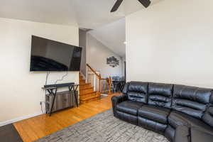 Living area featuring light wood finished floors, stairway, a ceiling fan, and lofted ceiling