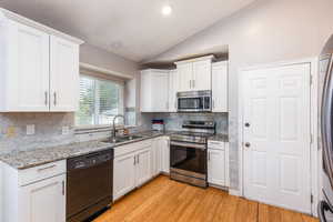Kitchen with appliances with stainless steel finishes, vaulted ceiling, white cabinetry, and recessed lighting