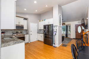 Kitchen featuring appliances with stainless steel finishes, light wood-style floors, decorative backsplash, white cabinetry, and recessed lighting