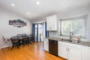 Kitchen with dishwasher, plenty of natural light, light stone countertops, white cabinets, and vaulted ceiling