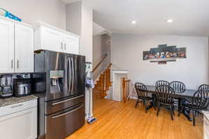 Kitchen with stainless steel fridge with ice dispenser, white cabinetry, light stone counters, light wood-type flooring, and recessed lighting