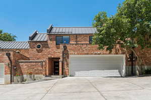 Front of property with a standing seam roof, concrete driveway, brick siding, a metal roof, and an attached garage
