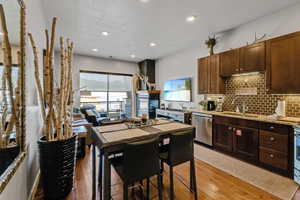 Kitchen featuring dishwasher, light wood finished floors, backsplash, light stone countertops, and dark brown cabinets