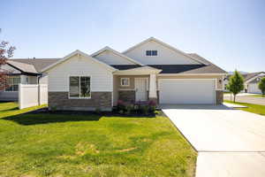 Craftsman inspired home with stone siding, an attached garage, concrete driveway, a front yard, and roof with shingles