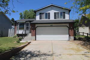 Tri-level home with brick siding, an attached garage, and driveway