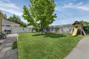 Fenced backyard with a trampoline, a playground, and a patio area