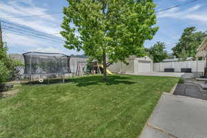 View of yard featuring a trampoline, concrete driveway, an outdoor structure, a playground, and a garage