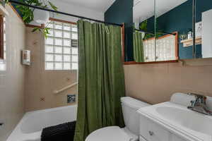 Full bathroom with shower / bath combo with shower curtain, vanity, and tile walls