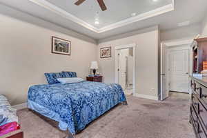 Bedroom featuring a raised ceiling, baseboards, crown molding, light colored carpet, and a ceiling fan