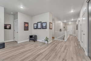 Hall with an upstairs landing, light wood-type flooring, baseboards, and a textured ceiling