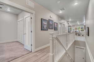 Hall with an upstairs landing, light wood finished floors, baseboards, and recessed lighting