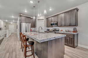 Kitchen featuring stainless steel appliances, baseboards, dark brown cabinetry, a sink, and backsplash