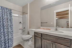 Full bath featuring vanity, shower / bath combo with shower curtain, toilet, and marble look tiles