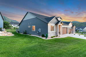 Property exterior at dusk with board and batten siding, concrete driveway, a mountain view, a garage, and a yard
