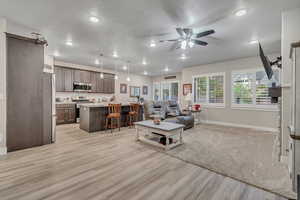 Living room featuring baseboards, light wood-type flooring, a textured ceiling, a ceiling fan, and recessed lighting