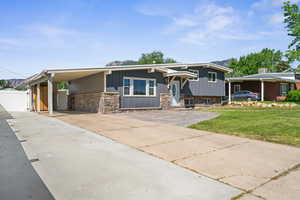 View of front facade featuring concrete driveway, stone siding, an attached carport, and a gate