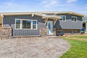 View of front of property featuring board and batten siding, a front yard, and stone siding