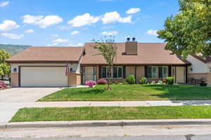 Ranch-style home featuring an attached garage, a front lawn, brick siding, and driveway