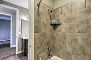 Bathroom view of  shower combination, wood finished floors, vanity, and baseboards