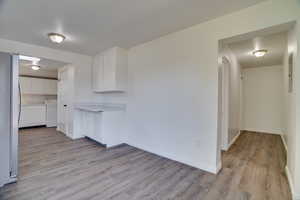 Kitchen featuring washer / clothes dryer, freestanding refrigerator, light wood finished floors, white cabinetry, and light countertops
