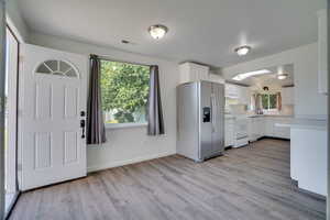 Kitchen with stainless steel fridge with ice dispenser, range, light countertops, under cabinet range hood, and light wood finished floors