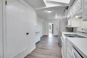Kitchen featuring white appliances, white cabinets, light countertops, light wood-type flooring, and under cabinet range hood