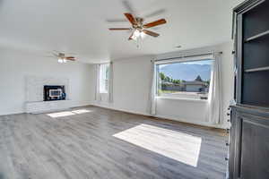 Unfurnished living room with ceiling fan, wood finished floors, and a glass covered fireplace