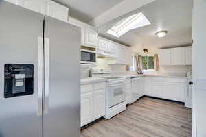 Kitchen featuring appliances with stainless steel finishes, a skylight, under cabinet range hood, white cabinets, and light wood-style floors