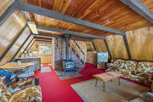 Carpeted living room with a wood stove, wooden ceiling, and wooden walls