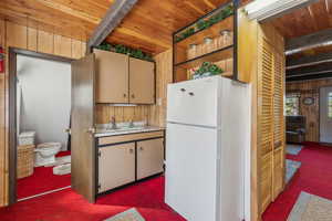 Kitchen featuring freestanding refrigerator, a wood ceiling with exposed beams, carpet, light countertops, and wooden walls