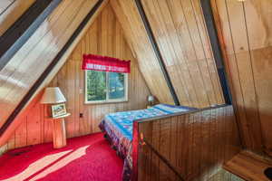 Bedroom with vaulted ceiling, wood walls, and carpet floors
