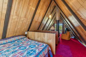 Bedroom featuring carpet flooring, wood walls, and lofted ceiling