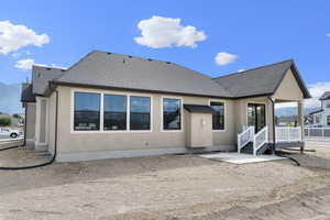 Rear view of property featuring roof with shingles, stucco siding, and a patio area