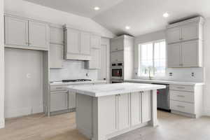 Kitchen featuring decorative backsplash, stainless steel appliances, vaulted ceiling, light stone counters, and a center island