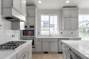 Kitchen with gray cabinets, decorative backsplash, recessed lighting, light stone countertops, and appliances with stainless steel finishes