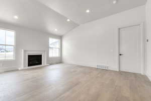 Unfurnished living room with lofted ceiling, light wood-style flooring, recessed lighting, and a fireplace with raised hearth