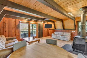 Living area featuring a wood stove, a wooden ceiling with exposed beams, wood walls, and wood finished floors