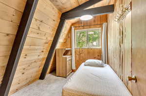 Carpeted bedroom with vaulted ceiling and wooden walls