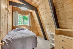 Bedroom featuring vaulted ceiling, wooden walls, and carpet