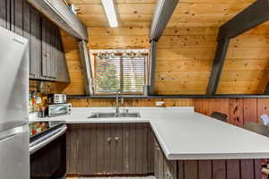 Kitchen featuring stainless steel appliances, light countertops, a wooden ceiling with exposed beams, and wood walls