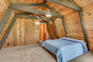 Carpeted bedroom with vaulted ceiling, wooden walls, and wood ceiling