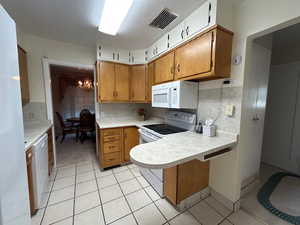 Kitchen featuring white appliances, light countertops, light tile patterned floors, a peninsula, and a chandelier