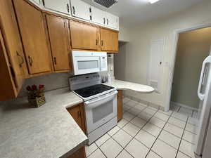 Kitchen with white appliances, light countertops, light tile patterned floors, and brown cabinetry