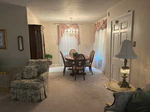 Dining area with a chandelier, light carpet, and a textured ceiling