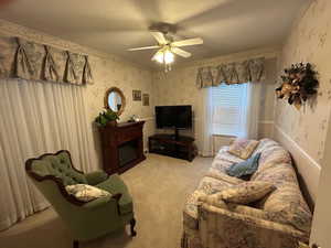 Living area featuring light colored carpet, a ceiling fan, wallpapered walls, and a glass covered fireplace