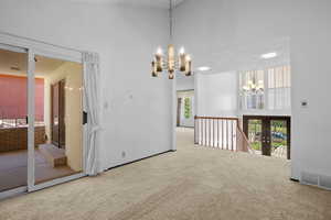 Carpeted empty room featuring a chandelier and a towering ceiling